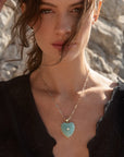 Woman wearing a necklace with a heart-shaped pendant against a stone wall background