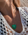Close-up of a person wearing a white crochet top with a green heart-shaped pendant necklace.