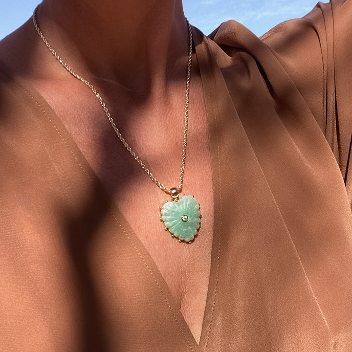 Necklace with a green heart-shaped pendant worn by a person in a brown garment.