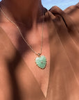 Necklace with a green heart-shaped pendant worn by a person in a brown garment.