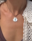 Person wearing a necklace with a shell pendant against a neutral background