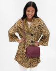 Woman wearing a leopard print coat with a purple handbag on a white background