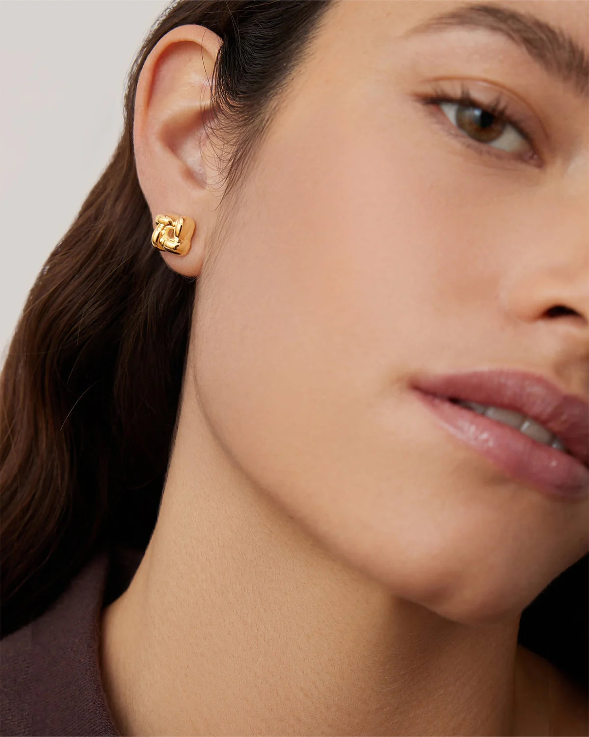Close-up of a person wearing gold earrings with a neutral background