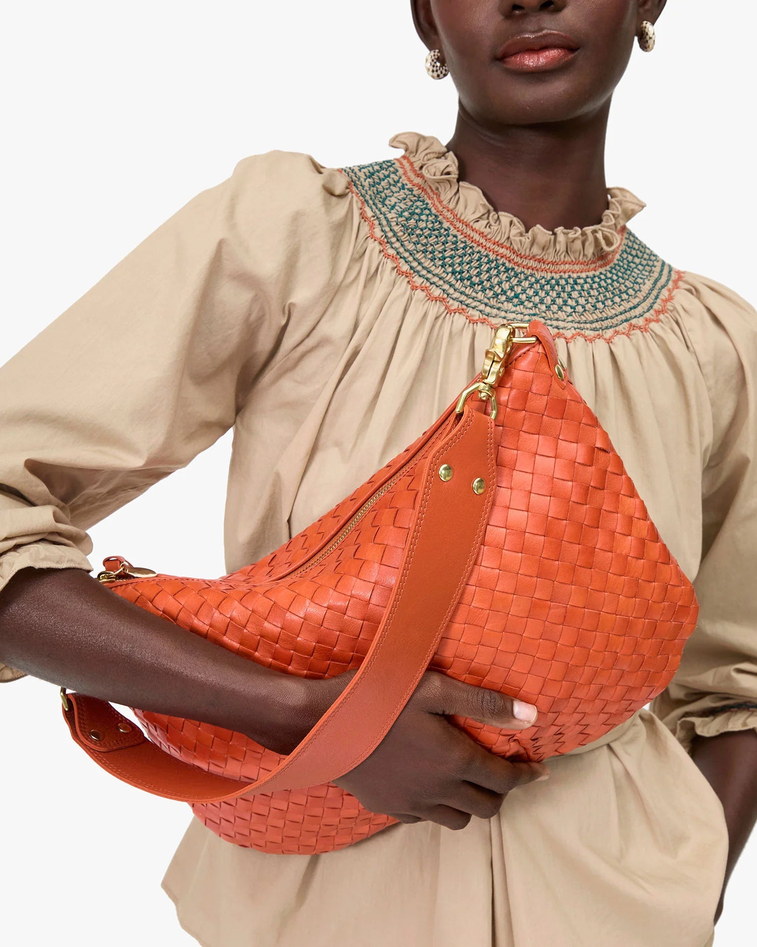 Person holding an orange woven handbag against a neutral background