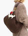 Person wearing a brown bag with a dog-themed keychain, on a plain background