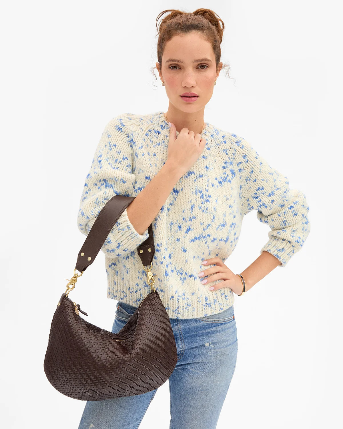 A woman modeling a cream and blue speckled knit sweater and light blue jeans, carrying a dark brown woven hobo shoulder bag with a brown strap and gold-tone hardware against a plain white background.