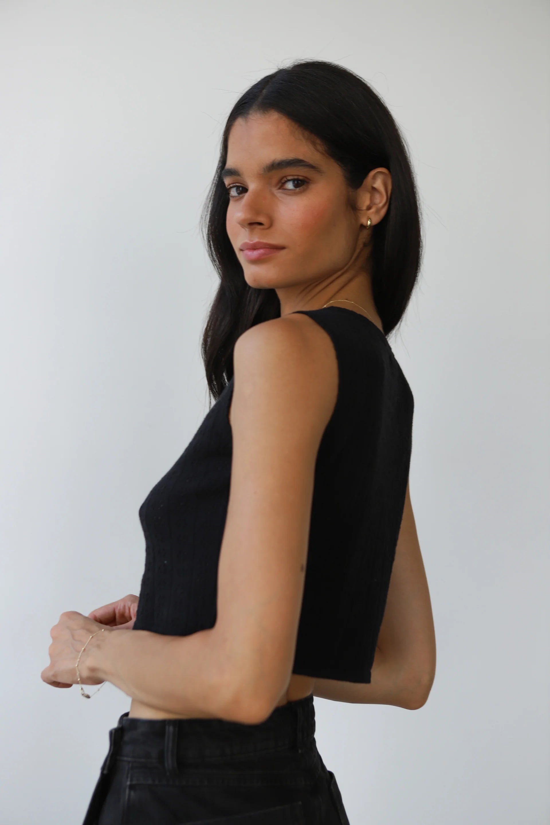 Woman wearing a black sleeveless top against a white background, back view