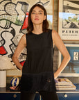 Woman in a black sleeveless top standing in front of a wall with artistic decorations.
