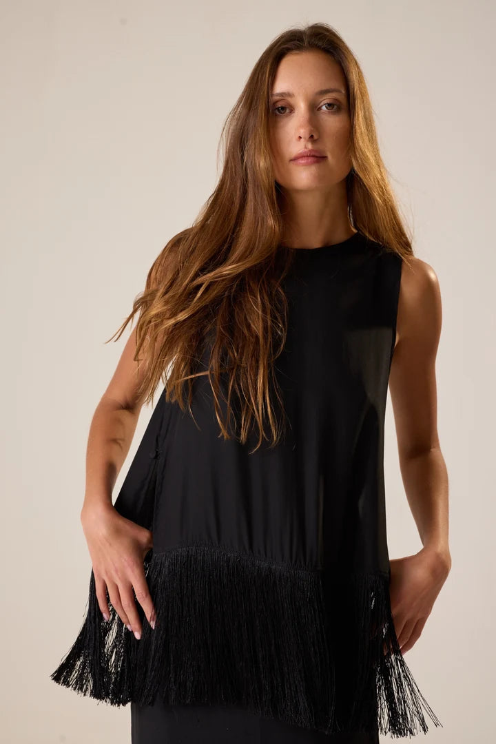 Woman wearing a black sleeveless top with fringe details against a plain background