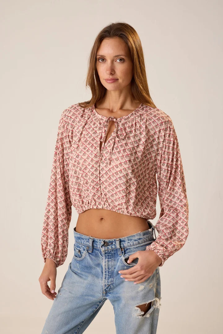 Woman wearing a patterned blouse and jeans against a plain background