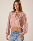 Woman wearing a patterned blouse and jeans against a plain background