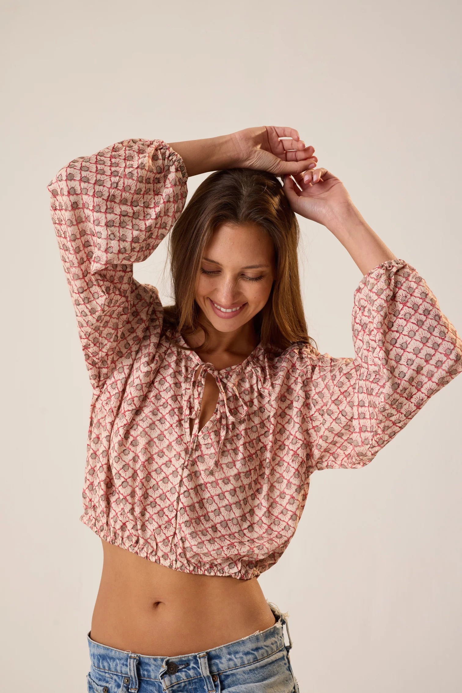 Woman wearing a pink patterned blouse and denim shorts against a plain background