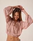 Woman wearing a pink patterned blouse and denim shorts against a plain background