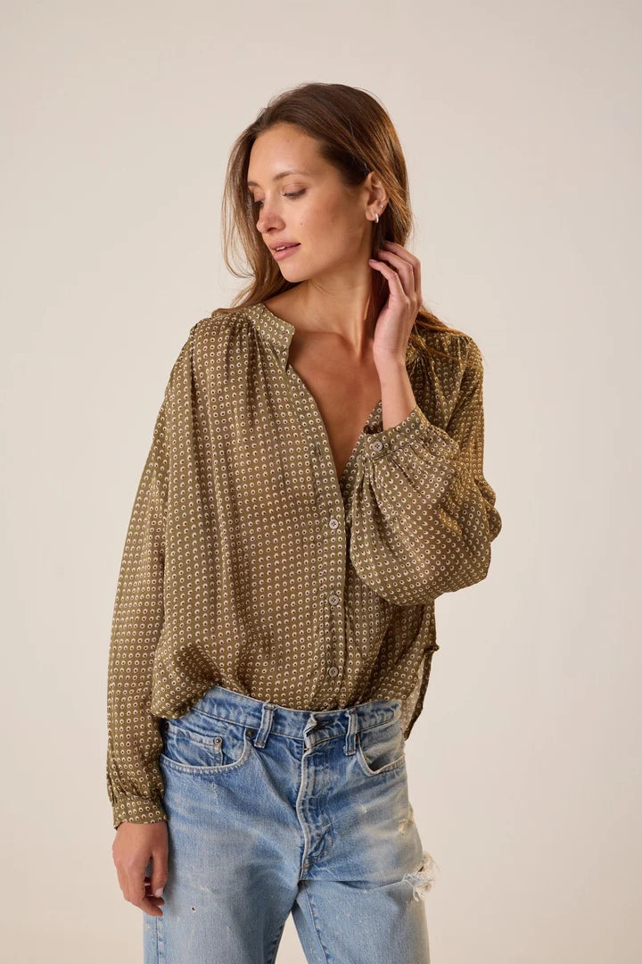 Woman wearing a patterned blouse and jeans against a plain background