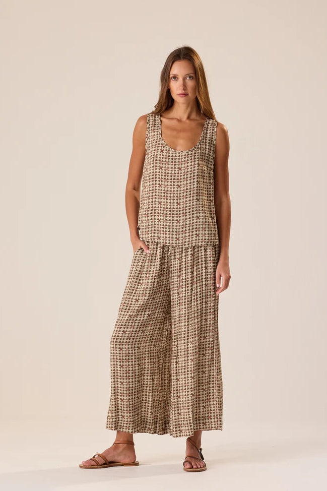 A woman modeling a sleeveless, wide-leg two-piece set in a brown and beige houndstooth pattern, standing against a solid light beige studio background.