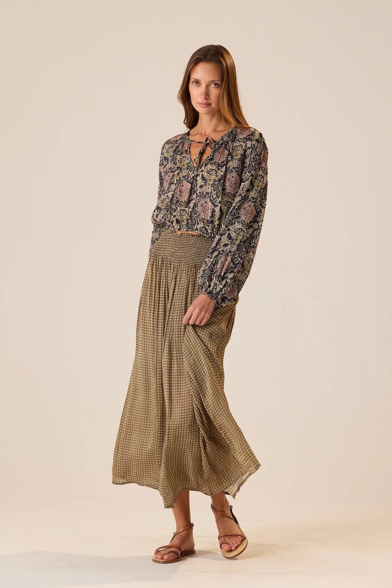 Woman wearing a patterned blouse and Bella Skirt Martini Olive on a beige background