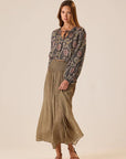 Woman wearing a patterned blouse and Bella Skirt Martini Olive on a beige background