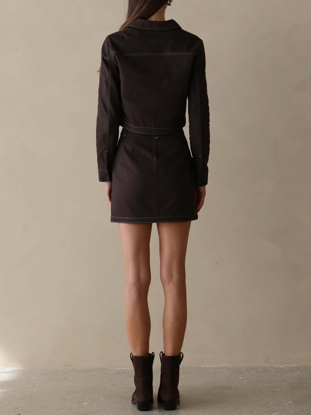 Person wearing a black dress with a belt against a beige background