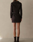 Person wearing a black dress with a belt against a beige background