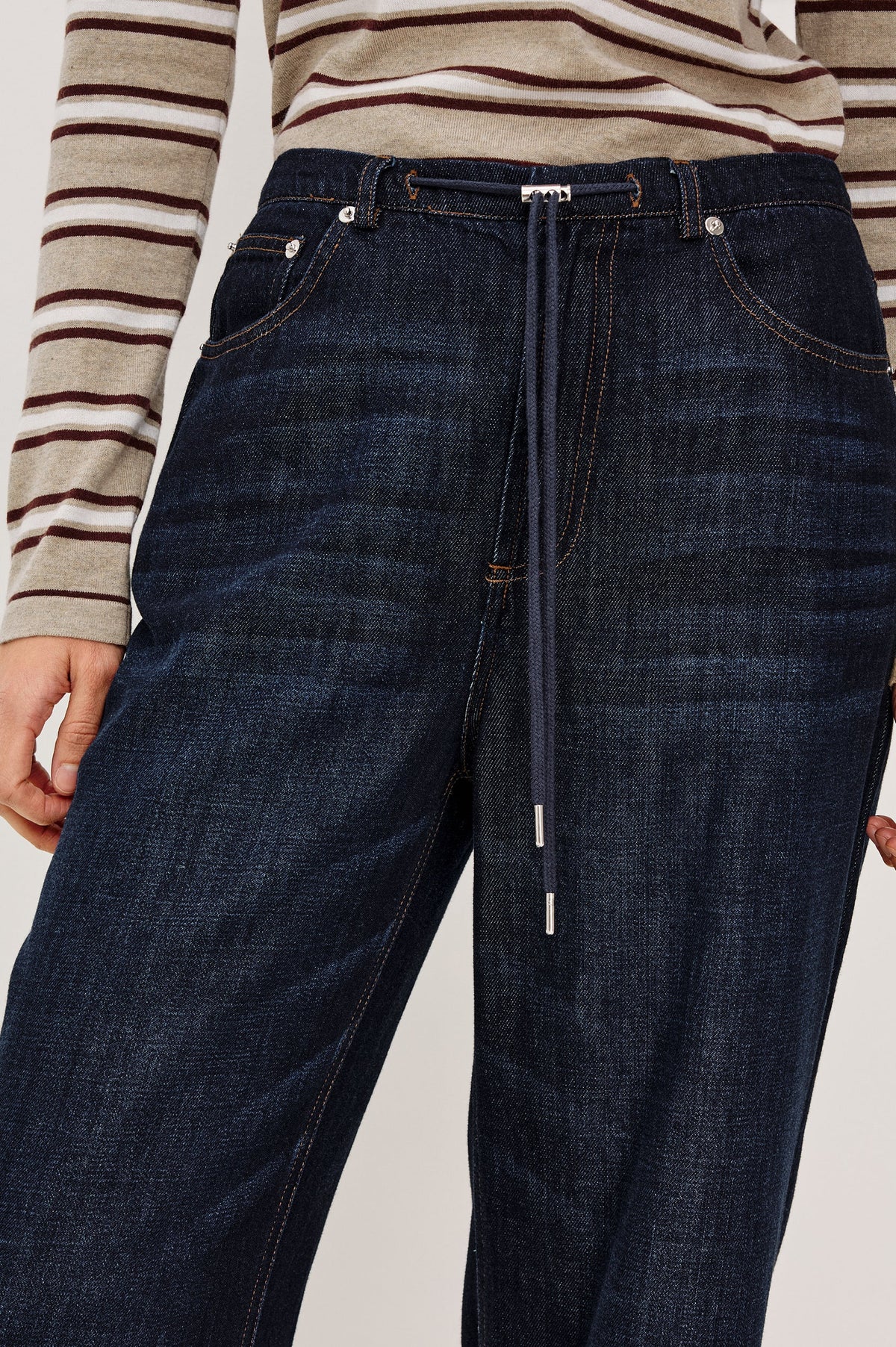 close up of a denim tie waist pant worn by a model with a stripe shirt on a grey background