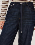 close up of a denim tie waist pant worn by a model with a stripe shirt on a grey background