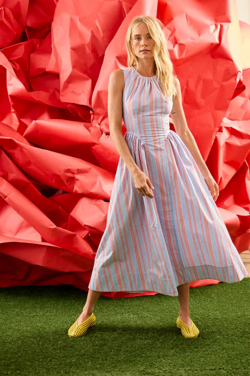 Woman in a striped dress standing in front of large red floral arrangements.