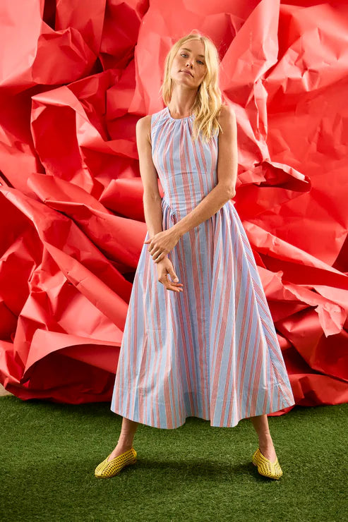 Woman in a striped dress standing in front of a large red flower-like structure.