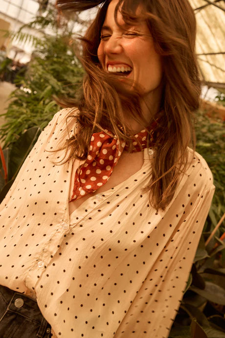 Woman laughing with a polka dot scarf around her neck, surrounded by greenery.