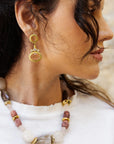 Close-up of a woman wearing gold earrings and a necklace with beads.