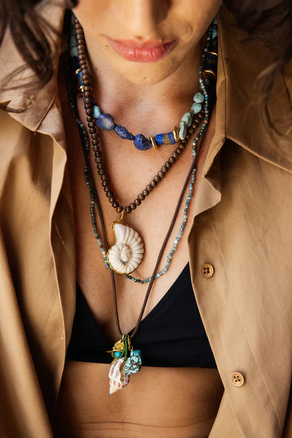 Close-up of a person wearing multiple necklaces with a beige jacket.