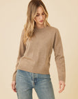 Woman wearing a brown sweater and blue jeans against a beige background