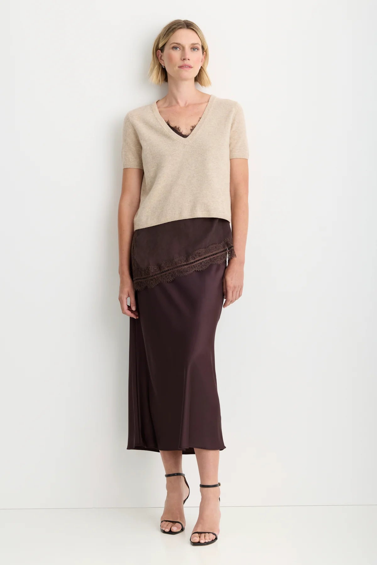 model wearing a oatmeal short sleeve sweater over a brown lace top and brown skirt on a white background 