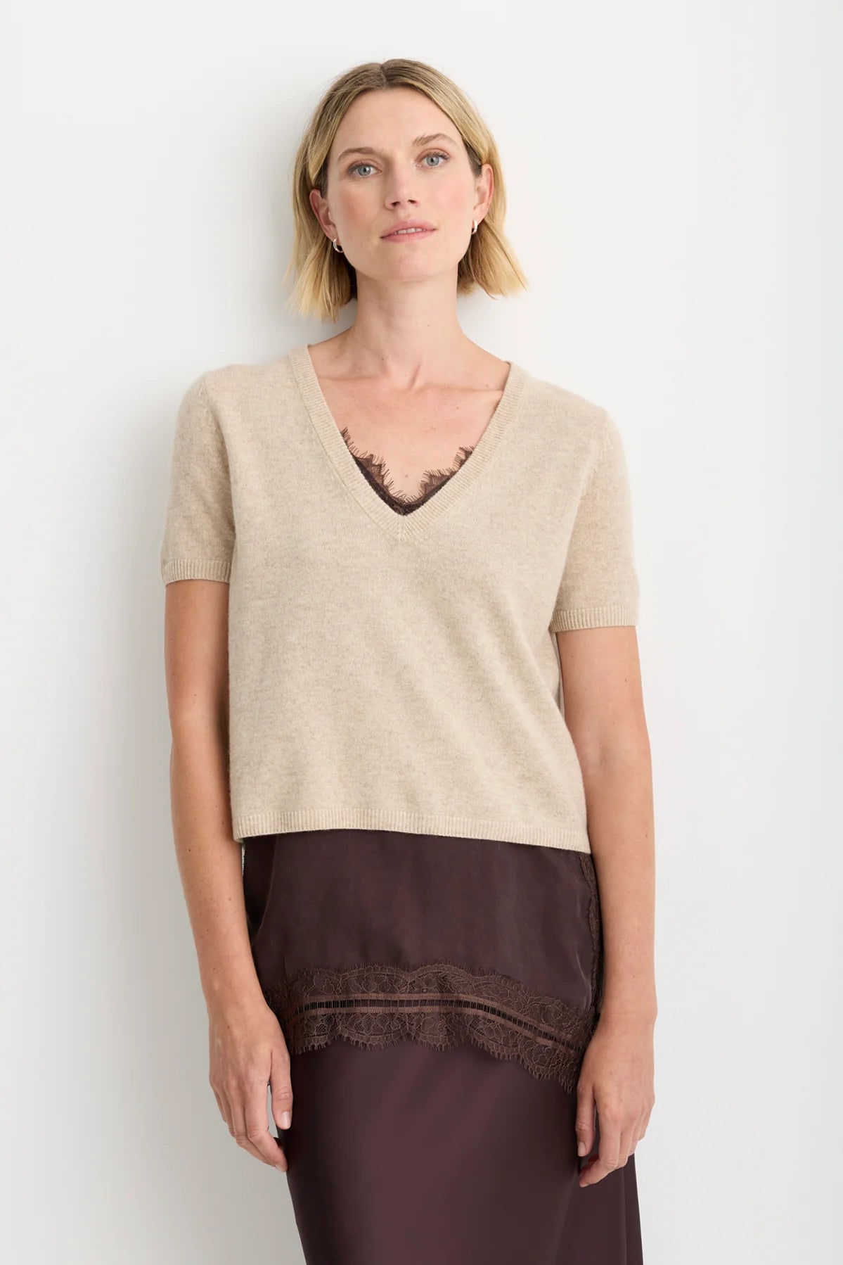 model wearing a oatmeal short sleeve sweater over a brown lace top and brown skirt on a white background 