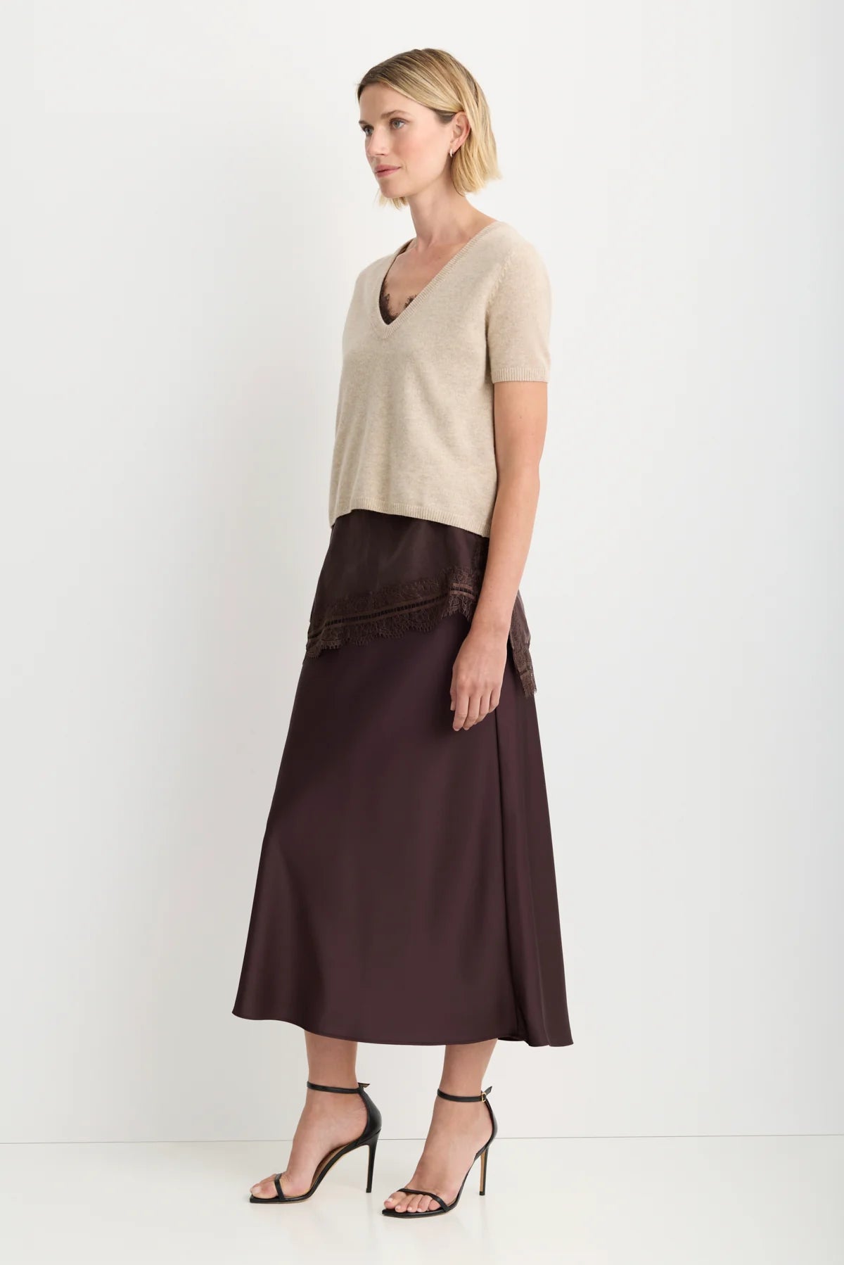 model wearing a oatmeal short sleeve sweater over a brown lace top and brown skirt on a white background, side view