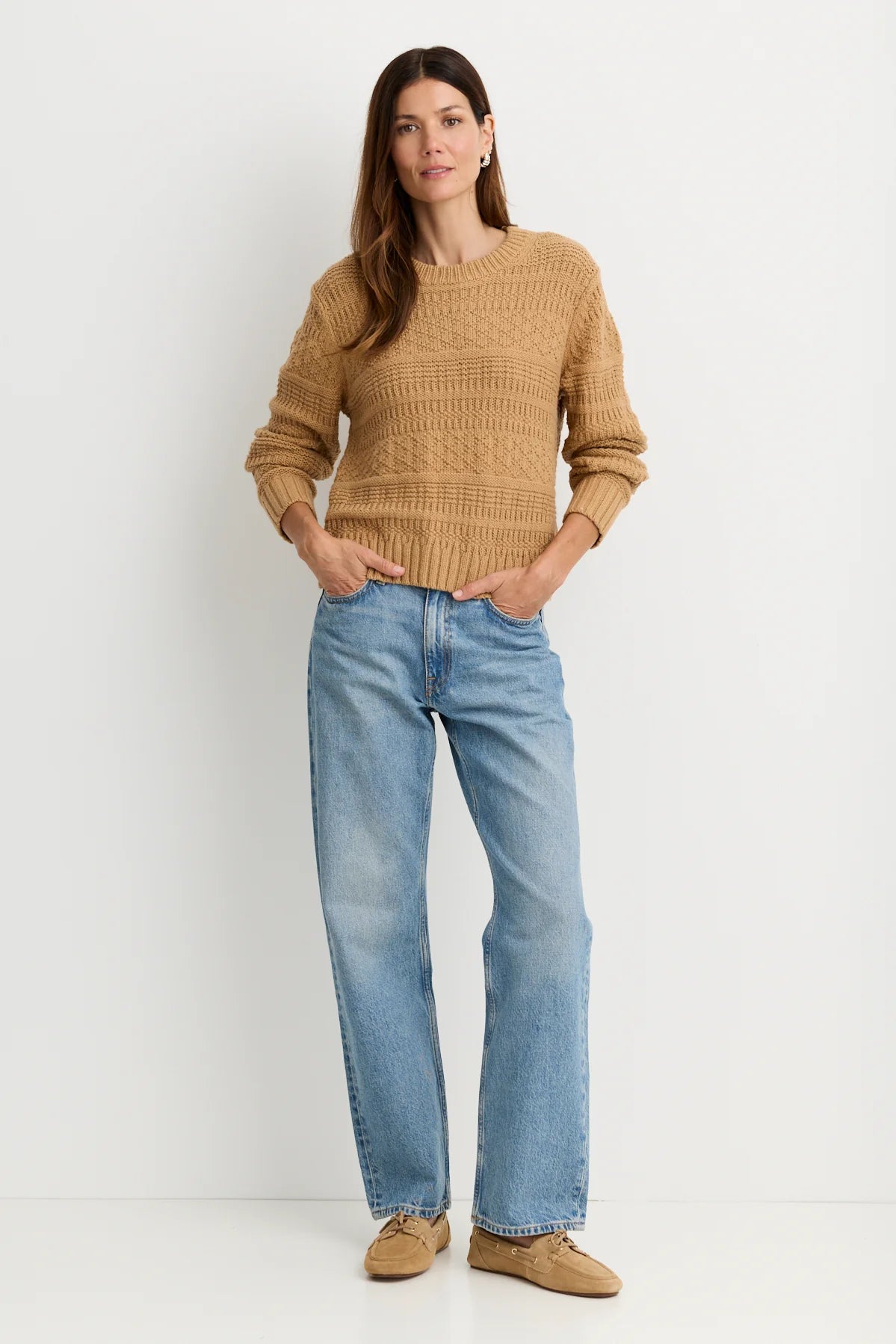 model wearing a tan sweater with blue jeans on a white background