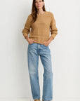 model wearing a tan sweater with blue jeans on a white background