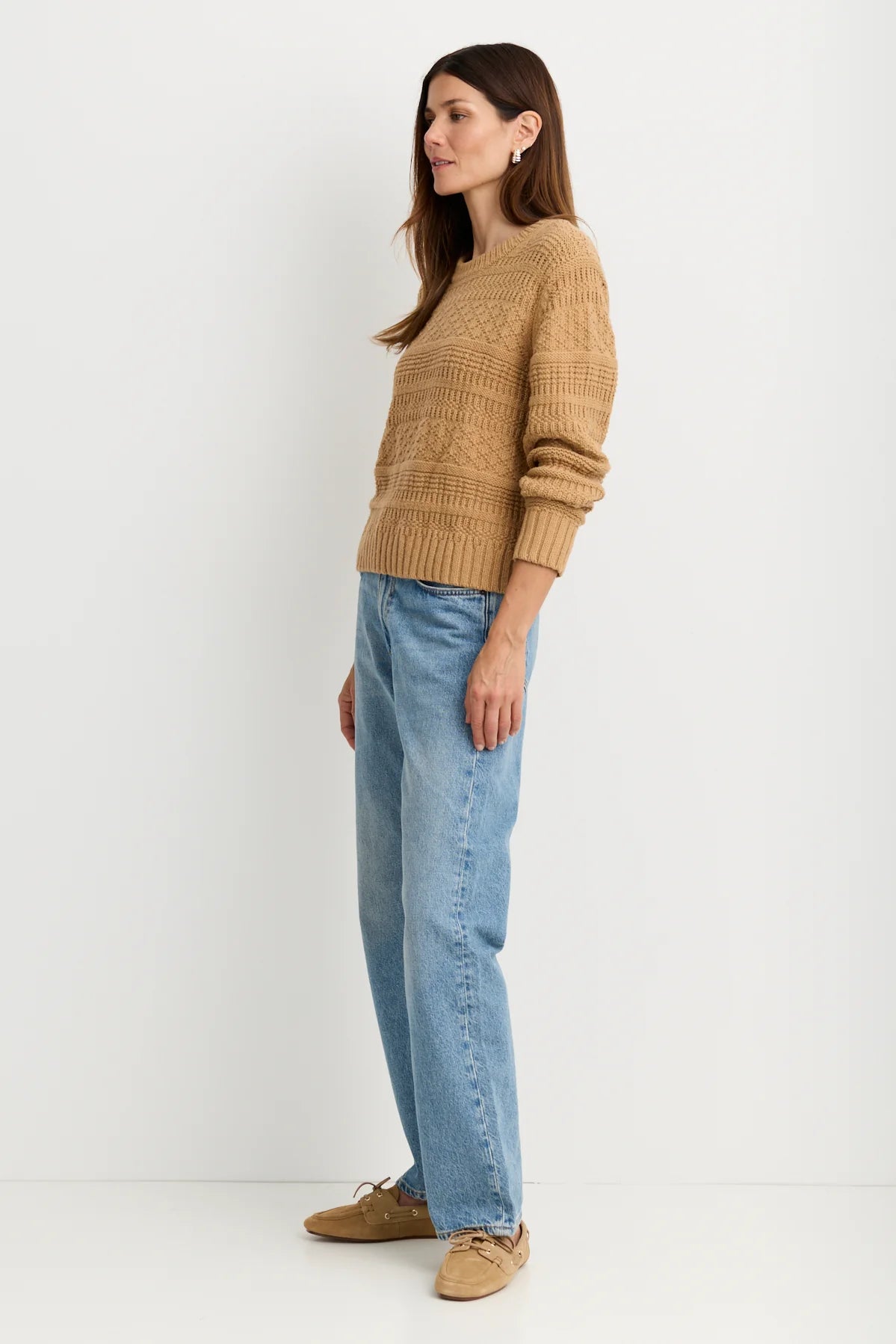 model wearing a tan sweater with blue jeans on a white background, side view