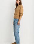 model wearing a tan sweater with blue jeans on a white background, side view