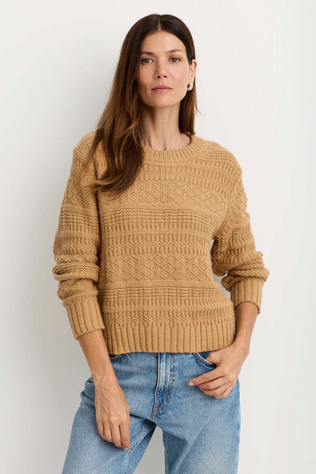 model wearing a tan sweater with blue jeans on a white background