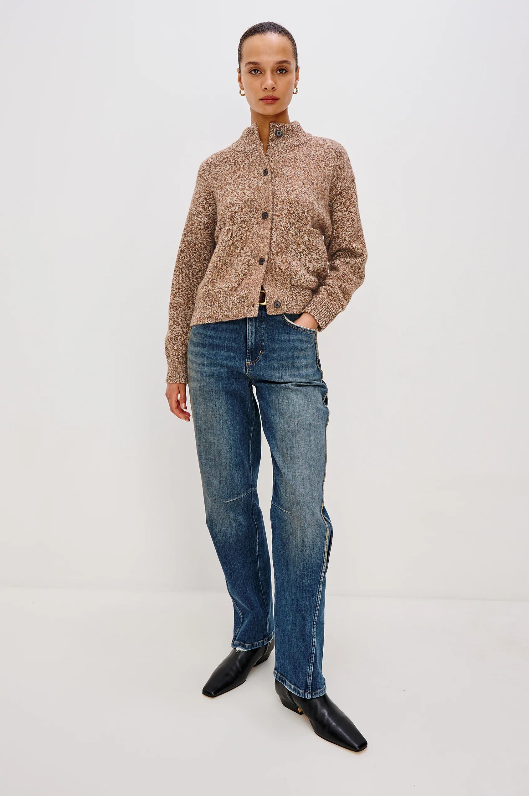 Person wearing a brown patterned jacket and blue jeans on a white background
