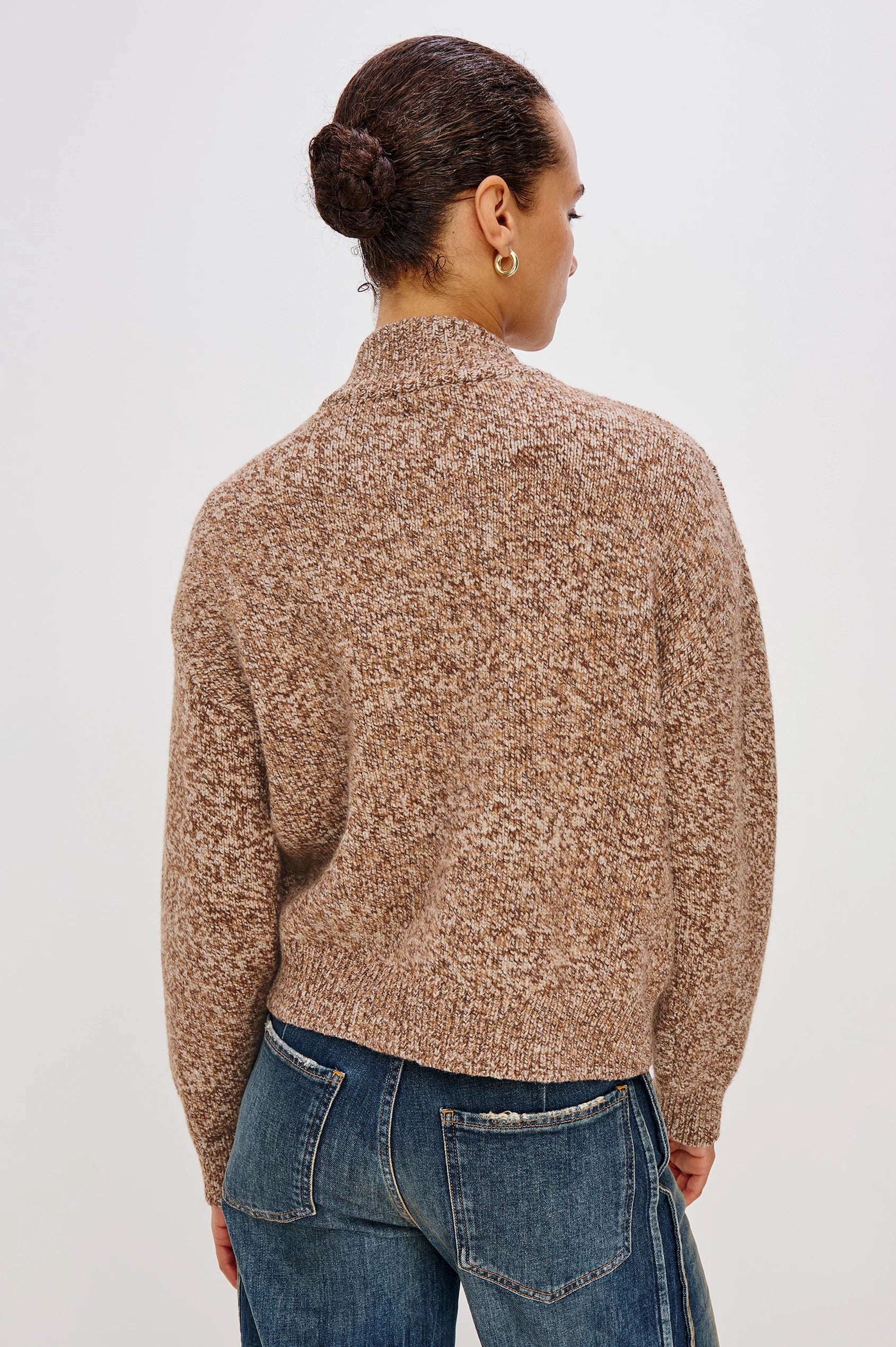 Person wearing a brown patterned sweater and blue jeans on a white background