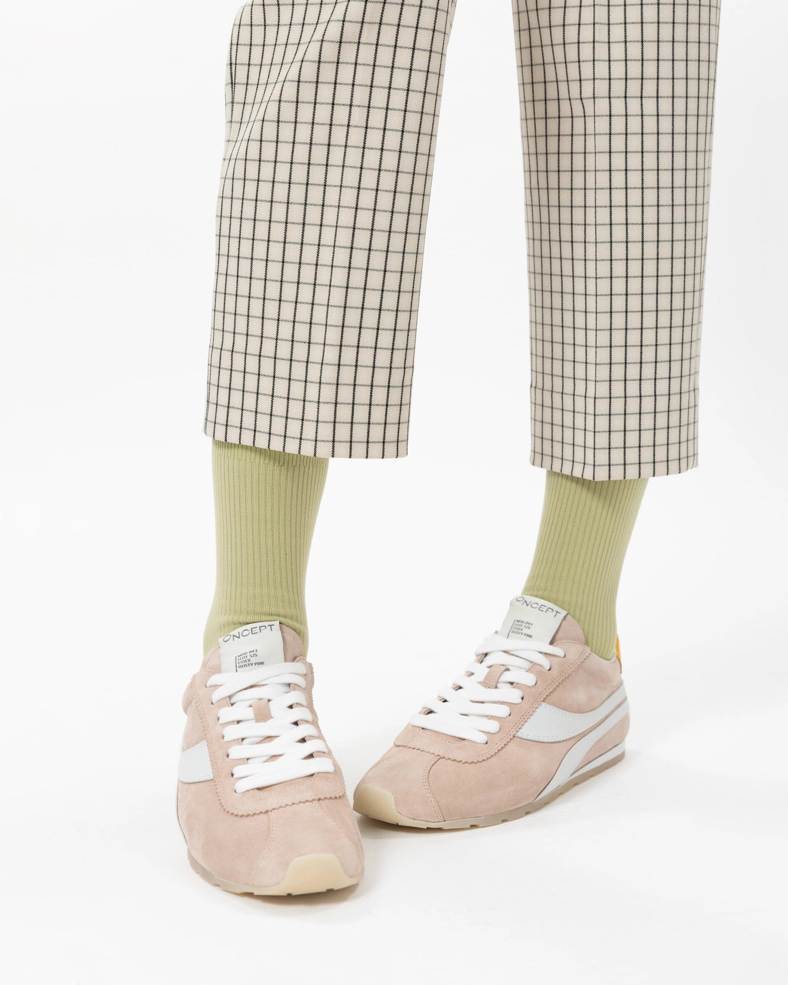 Person wearing checkered pants, light green socks, and pink sneakers on a white background