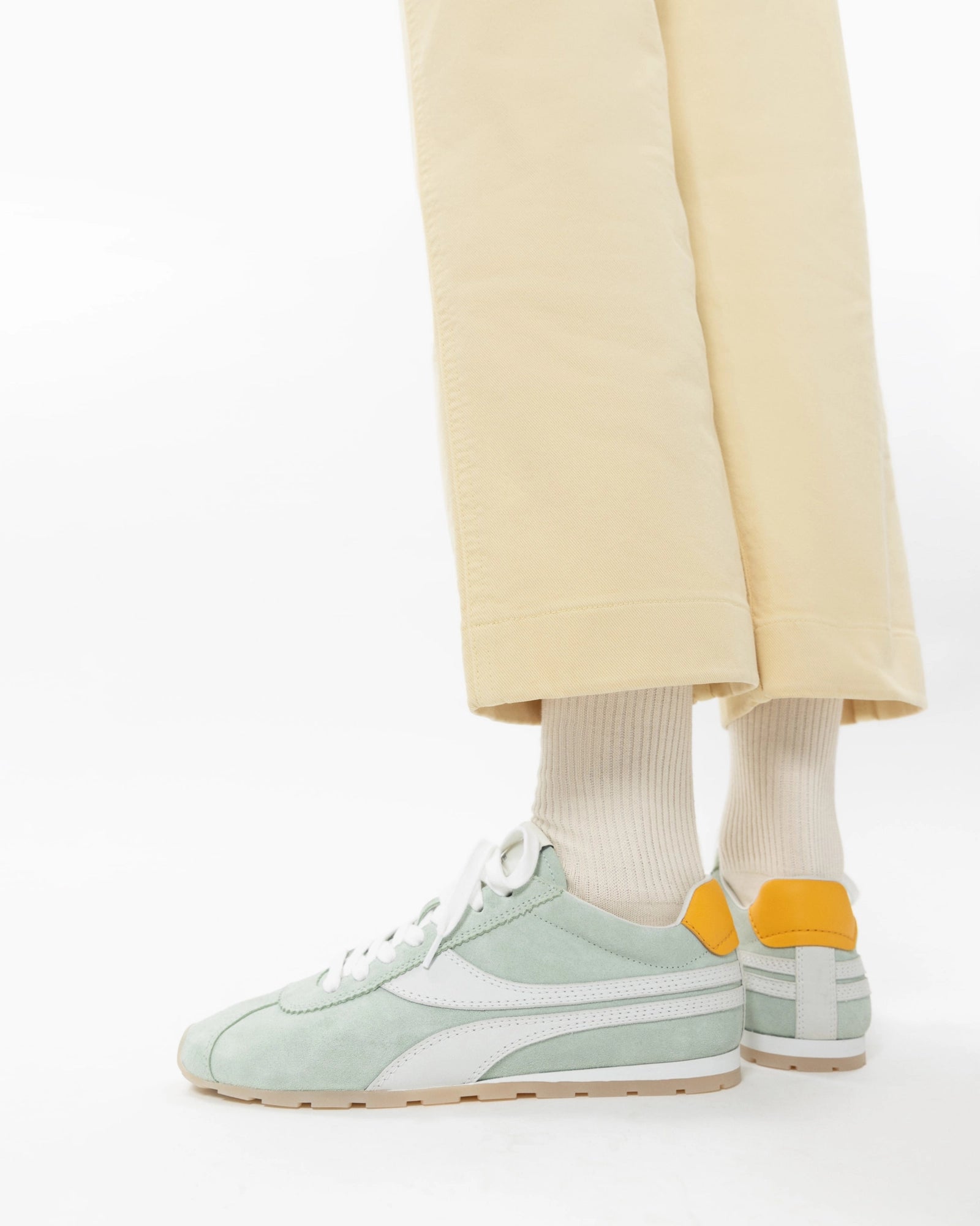 Light green sneakers worn with beige pants and white socks on a white background