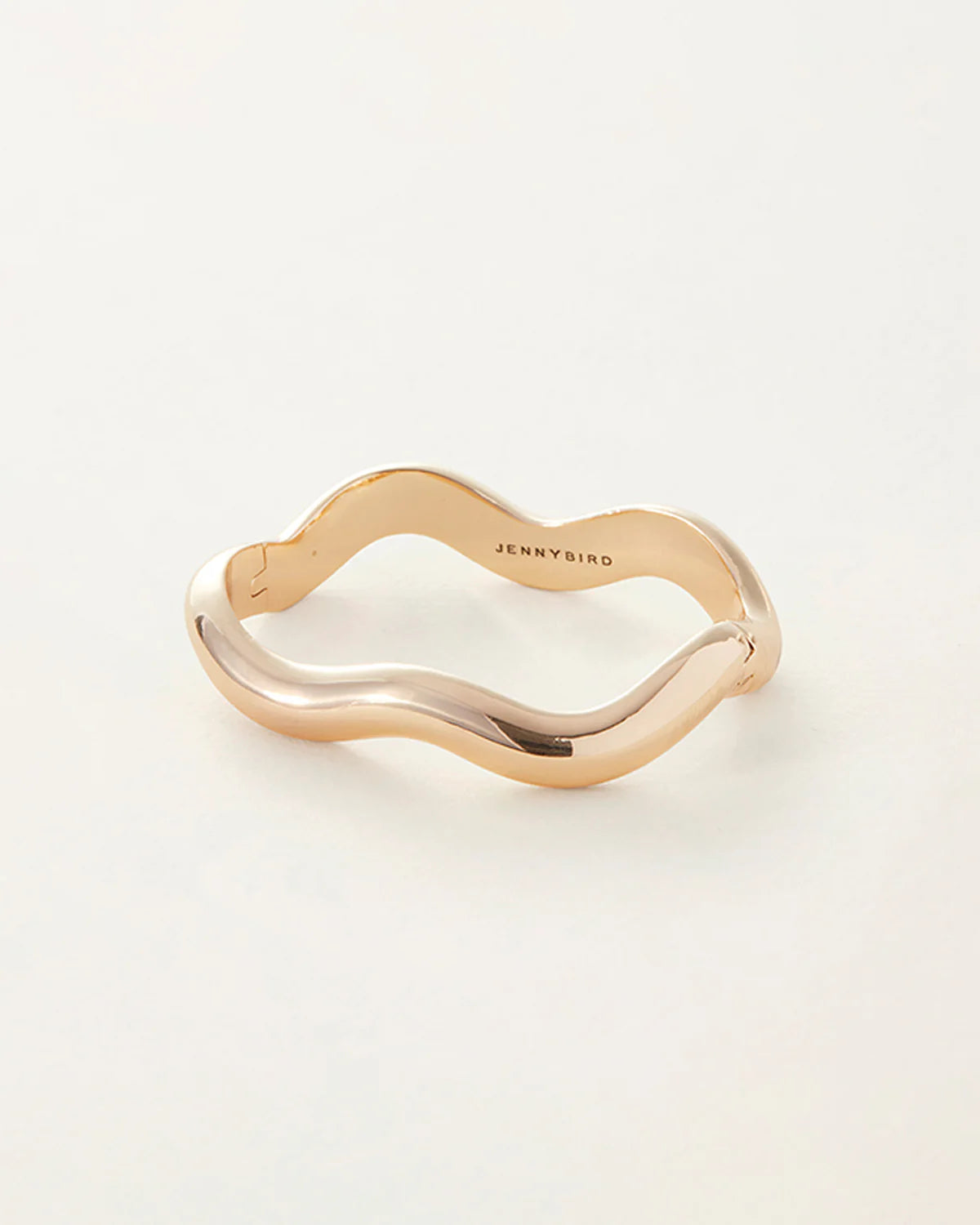 Gold ring with wavy design on a white background, branded 'Jenny Bird'.