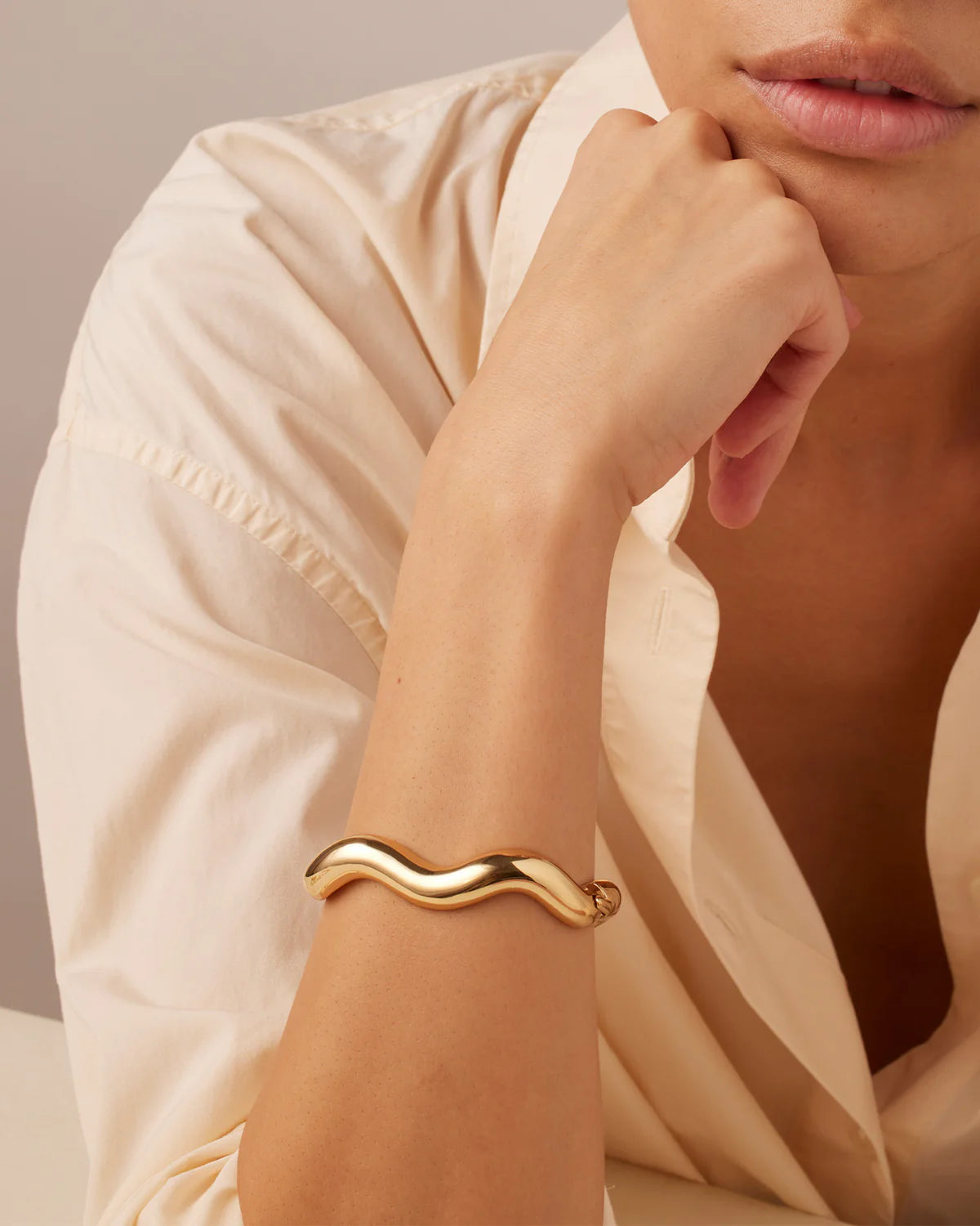 Gold bracelet on a person's wrist with a neutral background