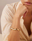 Gold bracelet on a person's wrist with a neutral background
