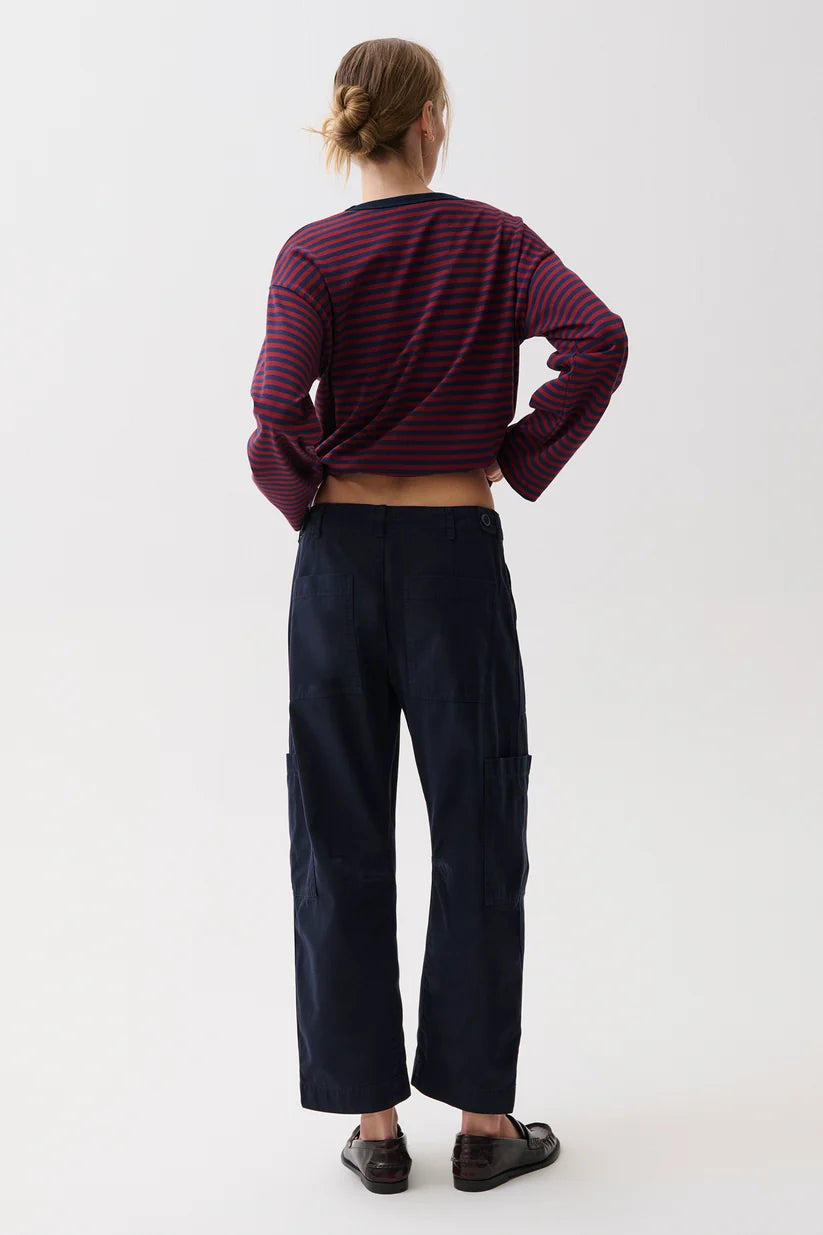 A model shown from the back wearing a cropped long-sleeve striped top in dark red and navy, paired with dark navy wide-leg pants and black shoes, against a plain white studio background.