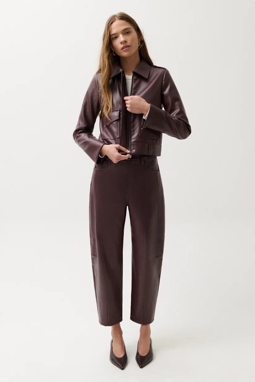 A woman modeling a dark brown faux leather jacket and matching wide-leg cropped trousers against a plain light gray studio background.