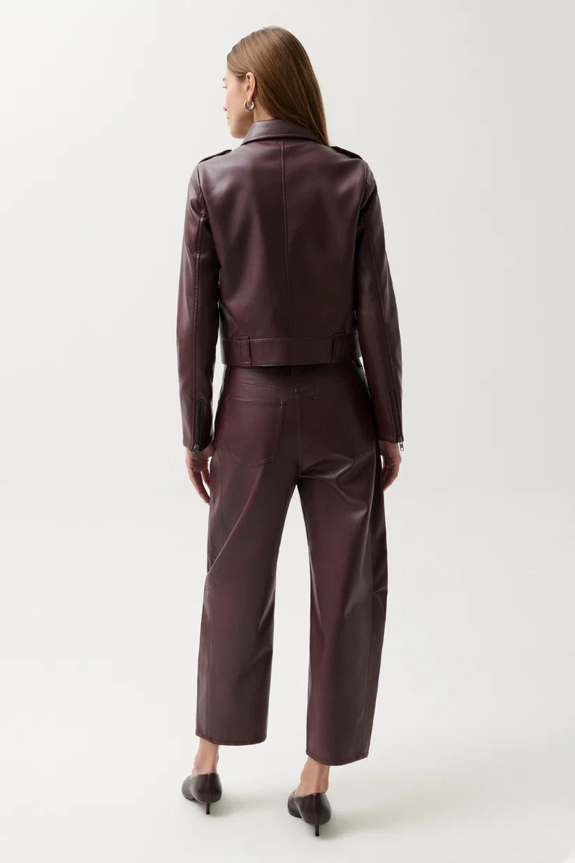 A woman viewed from the back wearing a dark plum faux-leather cropped jacket and matching wide-leg cropped pants, paired with dark pointed-toe heels, against a light gray studio background.
