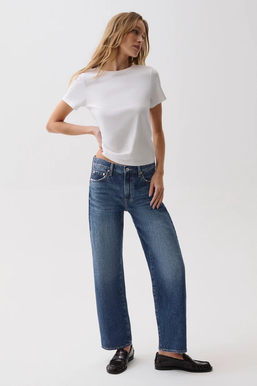 A woman modeling a white short-sleeve t-shirt and blue wide-leg jeans with black loafers, standing against a plain white studio background.